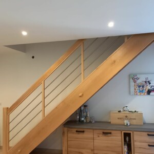 Escalier droit en hêtre avec contremarches et limons . Garde corps poteaux droits, main courante arrondie sur le dessus et 3 lisses inox intermédiares. Finition teinte et vernis.
